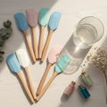 Flat lay of silicone mixing spatulas beside a glass beaker on wooden surface